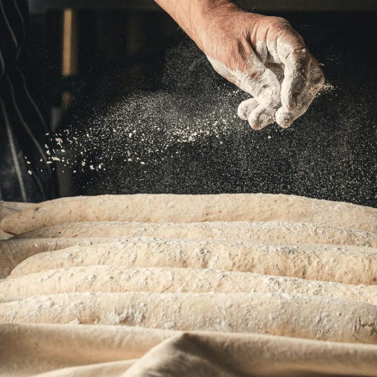Harinas LA ENCARNACIÖN para panaderos Mano espolvoreando harina sobre masa de pan en una superficie de trabajo.