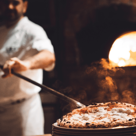 Harinas especiales para pizzerias Chef sacando una pizza del horno de leña con una pala.